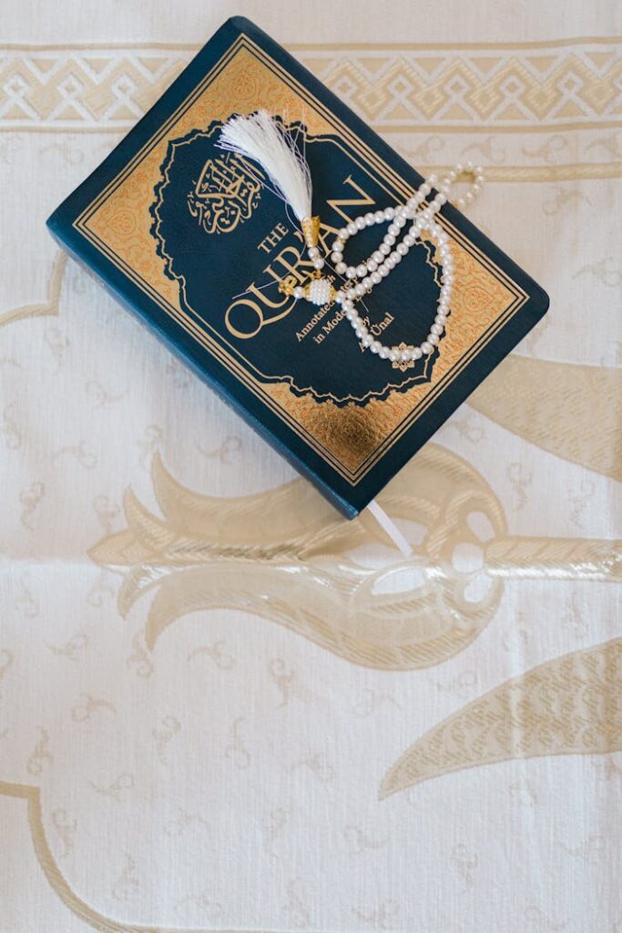 Top view of an elegant Quran and prayer beads on ornate white cloth, symbolizing Islamic faith.