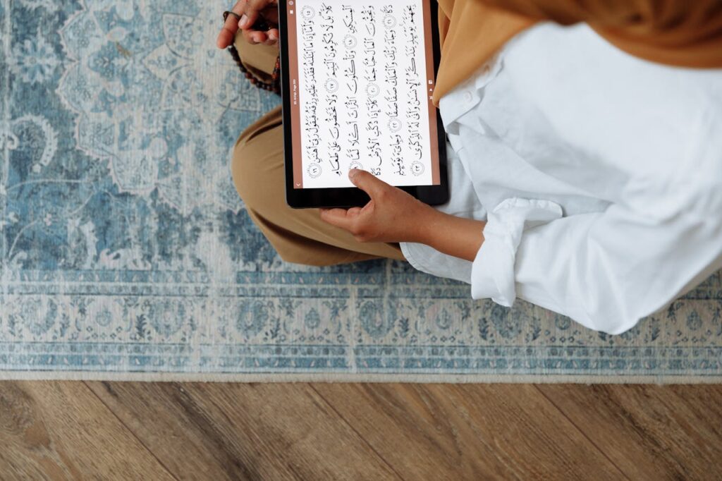 A woman in traditional wear reads Quran on tablet indoors. Perfect for cultural and religious themes.